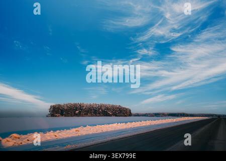 Eine verschneite Straße führt durch ein gefrorenes Feld unter einem schroffen Himmel. Stockfoto