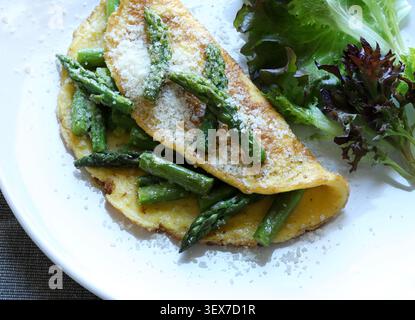 Hausgemachtes Spargel- und Parmesan-Omelette serviert mit frischem grünen Salat auf einem weißen Teller. Draufsicht. Stockfoto