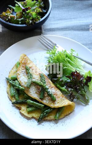 Hausgemachtes Spargel- und Parmesan-Omelette serviert mit frischem grünen Salat auf einem weißen Teller. Draufsicht. Stockfoto