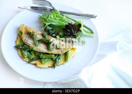 Hausgemachtes Spargel- und Parmesan-Omelette serviert mit frischem grünen Salat auf einem weißen Teller. Draufsicht. Stockfoto