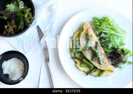 Hausgemachtes Spargel- und Parmesan-Omelette serviert mit frischem grünen Salat auf einem weißen Teller. Draufsicht. Stockfoto