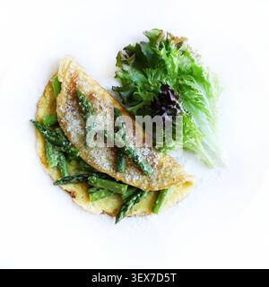 Hausgemachtes Spargel- und Parmesan-Omelette serviert mit frischem grünen Salat auf einem weißen Teller. Draufsicht. Stockfoto