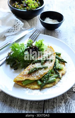 Hausgemachtes Spargel- und Parmesan-Omelette serviert mit frischem grünem Salat auf einem weißen Teller auf einem rustikalen Holzhintergrund. Stockfoto