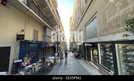 Eine enge Straße mit Geschäften und Leuten, die bei Tageslicht gesellig sind und eine lebhafte Szene schaffen, Valletta, Malta Stockfoto