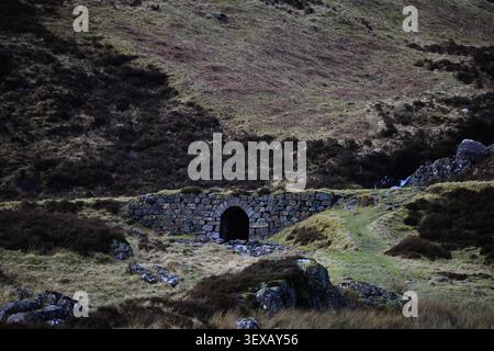 Three Sisters of Glencoe Area in den schottischen Highlands, Schottland, zeigt Steinhütten, felsigen Bach, Grasufer und dunkle Hügel über den Rahmen. Stockfoto