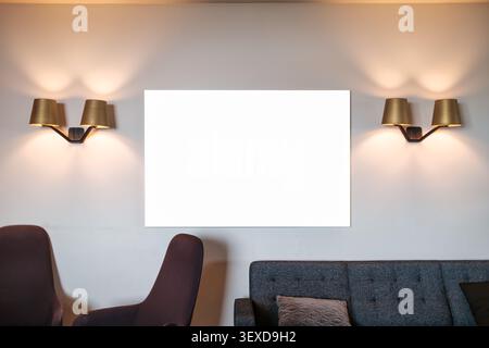 Zeitgenössischer skandinavischer gemütlicher Lounge-Bereich mit weißem Bilderrahmen, Messinglampen an der Wand und modernen Möbeln in warmer Atmosphäre Stockfoto