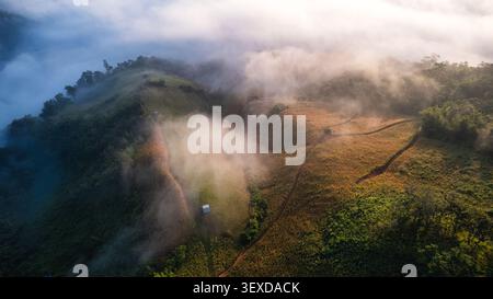 Blick aus der Vogelperspektive auf den nebeligen Morgen über ein hügeliges Feld mit üppig grünen Waldhängen und kargem Ackerland im ländlichen Südostasien Stockfoto