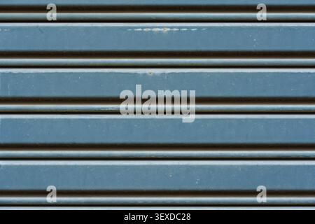 Blau und grau lackierte Metall Rollladen Garagentor Oberfläche mit gewellten Reihen subtile Rostflecken und abgenutzte Farbe industrielle Textur Hintergrund Stockfoto