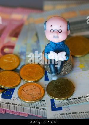 Ältere Figur auf Euro-Münzen mit Banknoten zur Darstellung von Renteneinsparungen und Rentenfinanzierung heute Stockfoto
