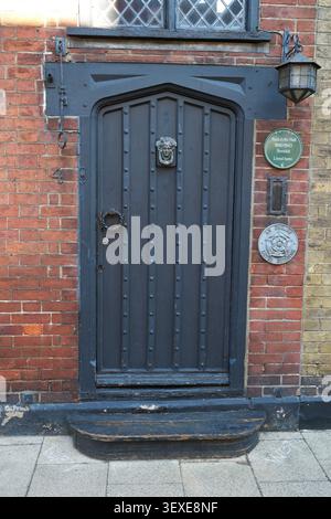 Nahaufnahme einer verzierten schwarzen Holztür mit Messingklopfer an der roten Ziegelwand. Stockfoto