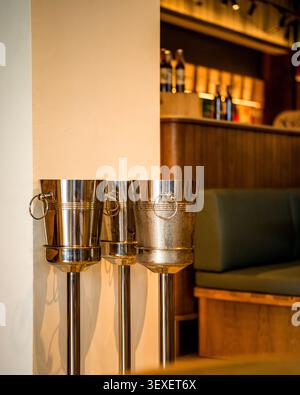 Weineisbehälter aus poliertem Edelstahl auf hohen Ständen, die an einer Wand in einem eleganten Restaurant angeordnet sind. Stockfoto