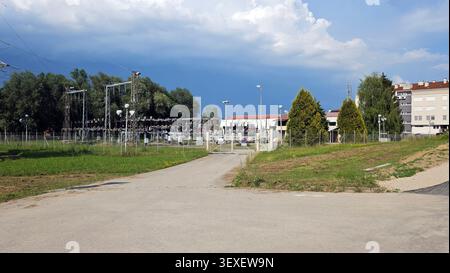Eine Umspannstation im Außenbereich verfügt über einen sicheren umzäunten Umkreis und Metalltore, die mit einer Asphaltzufahrt unter einem wolkenblauen Himmel verbunden sind Stockfoto