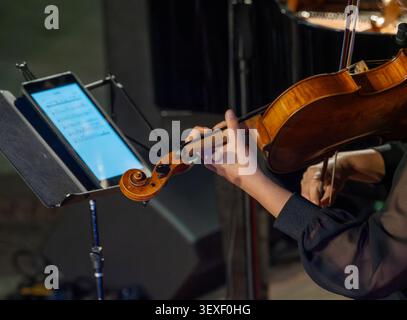 Der Musiker hält Bratsche, während er auf einem Konzert spielt. Die Hände passen das Gerät mit Sorgfalt und Präzision an. Der Notenständer zeigt brillante digitale s an Stockfoto