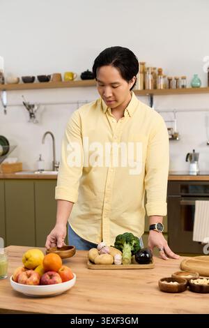 Asiatischer junger Mann bereitet frisches Gemüse in seiner stilvollen Küche für eine gesunde Mahlzeit zu Stockfoto