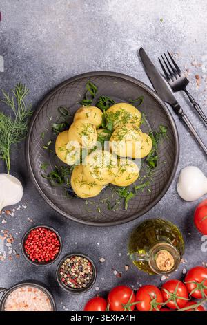 Neue Kartoffeln, die als gesunde Beilage zubereitet werden, mit frischem grünem Dill und Olivenöl gewürzt und heiß mit natürlichem Gemüse und Gewürzen auf einem Rusti serviert werden Stockfoto