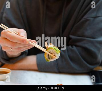 Eine Nahaufnahme einer kalifornischen Rolle, die von Stäbchen gehalten wird, mit wunderschöner Präsentation und kunstvoller Beschichtung. Das appetitliche Arrangement betont frische Zutaten und das sorgfältige Styling japanischer Speisen Stockfoto