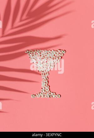 Sommerkomposition mit Martini-Glasform aus dekorativen Kristallen mit Palmblattschatten auf pastellrosa Hintergrund. Stockfoto