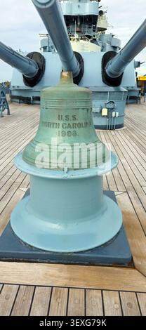 Wilmington, North Carolina, USA - 24. August 2025: Blick auf die Schiffsglocke auf dem Deck des Schlachtschiffes North Carolina, mit Geschütztürmen VIS Stockfoto