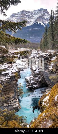 Athabasca Falls im Winter, Jasper National Park, Alberta, Kanada, teilweise gefrorener Wasserfall mit fließendem Wasser und schneebedeckter Bergkulisse. Stockfoto