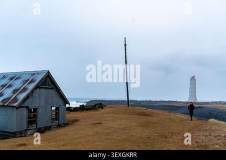 Eine einsame Wellblechkabine mit einem rostigen Dach steht an einem kargen grasbewachsenen Ufer in Island und blickt auf mächtige Meereswellen, die während einer kalten, überdeckten Jahreszeit abstürzen Stockfoto