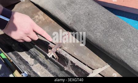 Eine Nahaufnahme einer Hand, die auf eine rostige Metallhalterung auf einer alten Dachkonstruktion zeigt. Stockfoto