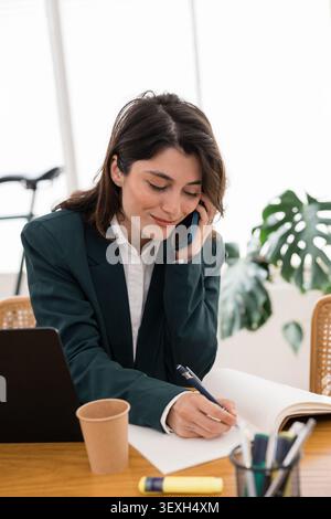 Junge Geschäftsfrau, die telefoniert und Notizen schreibt Stockfoto