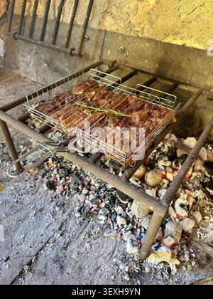 Nahaufnahme des Grillens über glühenden Kohlen auf einem rustikalen Grill im Freien, der traditionelle Gerichte und rauchige Aromen hervorhebt. Stockfoto