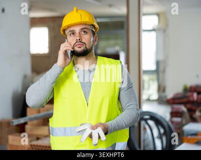 Junger bärtiger Bauingenieur, der auf der Baustelle telefoniert Stockfoto