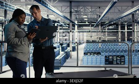 Das Engineering-Team des Rechenzentrums verwendet einen Laptop und ein Tablet in einem Serverraum, um die Testergebnisse zu überprüfen und den zuverlässigen Systembetrieb zu bestätigen. Stockfoto