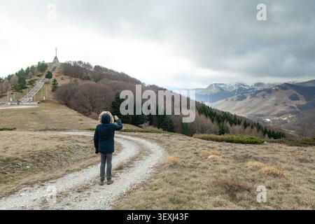 Ein Wanderer steht auf einem gewundenen Schotterweg und bewundert die zerklüftete Bergwilde, dunkle Wälder und dramatische schneebedeckte Gipfel. Blick vom Monte Zurro Stockfoto