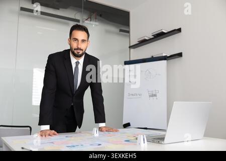 Porträt eines Geschäftsmannes, der sich mit bedruckten Materialien auf den Schreibtisch lehnt Stockfoto