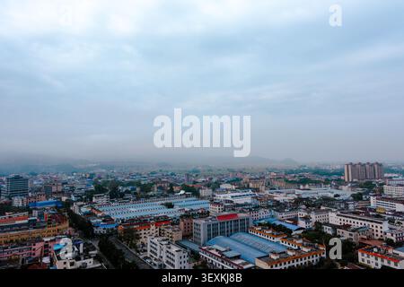 Eine breite Skyline der Stadt unter einem bewölkten blauen Himmel mit weichem Dunst, die dichte Gebäude, Straßen und eine ruhige urbane Atmosphäre von einem erhöhten Blick zeigt. Stockfoto