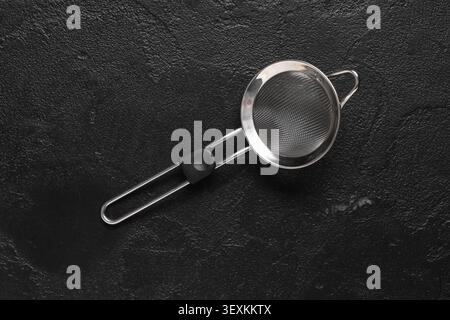 Teesieb aus Metall auf schwarz strukturierter Oberfläche Stockfoto