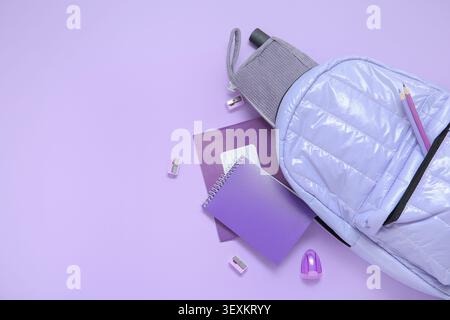Lila Schulrucksack mit verschiedenen Schreibwaren auf lila Hintergrund Stockfoto