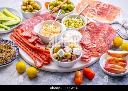 Eine wunderschön gestaltete Platte mit einer Auswahl an herzhaftem Fleisch, salzigen Oliven, cremigen Dips und knusprigem Obst, perfekt für Partys oder Picknicks Stockfoto