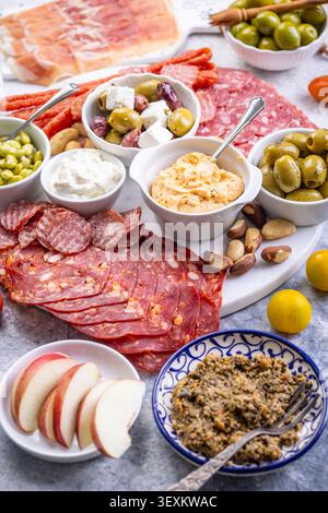 Eine wunderschön gestaltete Platte mit einer Auswahl an herzhaftem Fleisch, salzigen Oliven, cremigen Dips und knusprigem Obst, perfekt für Partys oder Picknicks Stockfoto