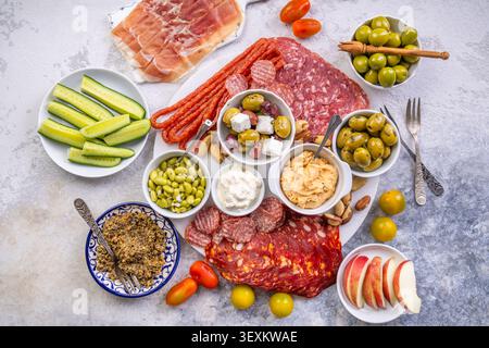 Eine wunderschön gestaltete Platte mit einer Auswahl an herzhaftem Fleisch, salzigen Oliven, cremigen Dips und knusprigem Obst, perfekt für Partys oder Picknicks Stockfoto