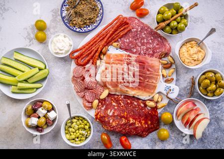 Eine wunderschön gestaltete Platte mit einer Auswahl an herzhaftem Fleisch, salzigen Oliven, cremigen Dips und knusprigem Obst, perfekt für Partys oder Picknicks Stockfoto