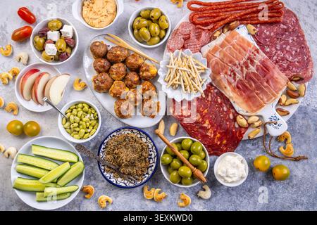 Eine wunderschön gestaltete Platte mit einer Auswahl an herzhaftem Fleisch, salzigen Oliven, cremigen Dips und knusprigem Obst, perfekt für Partys oder Picknicks Stockfoto