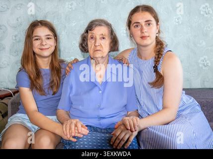 Großmutter mit zwei Enkelinnen, die auf einer Couch sitzen und Unterstützung und Zuneigung zeigen Stockfoto