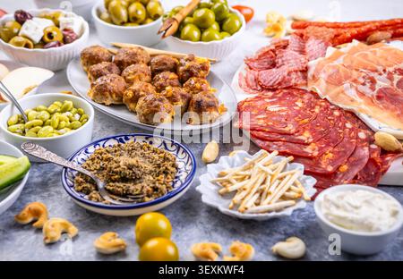 Eine wunderschön gestaltete Platte mit einer Auswahl an herzhaftem Fleisch, salzigen Oliven, cremigen Dips und knusprigem Obst, perfekt für Partys oder Picknicks Stockfoto