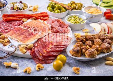 Eine wunderschön gestaltete Platte mit einer Auswahl an herzhaftem Fleisch, salzigen Oliven, cremigen Dips und knusprigem Obst, perfekt für Partys oder Picknicks Stockfoto