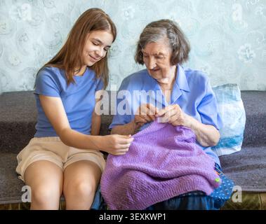 Großmutter bringt der Enkelin das Stricken bei, während sie zu Hause einen sanften Familienmoment teilt Stockfoto