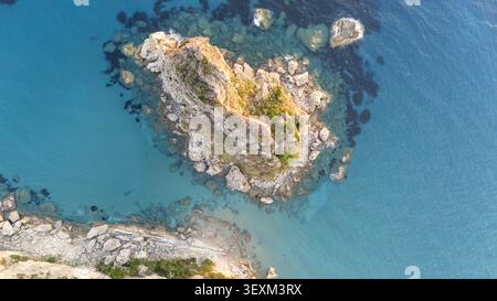 Blick aus der Vogelperspektive auf den Felsvorsprung von Paralia Fieroulas, umgeben von klarem türkisfarbenem Wasser und zerklüfteter Küste in Griechenland. Stockfoto