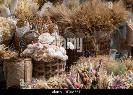 Getrocknete weiße Rosen und Weizengras in Korbkörben, die auf einem Kunsthandwerksmarkt ausgestellt werden Stockfoto