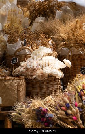Getrocknete weiße Rosen und Gerbera-Gänseblümchen in Korbkörben mit getrocknetem Weizen und Hasenschwanzgras auf einem Markt Stockfoto