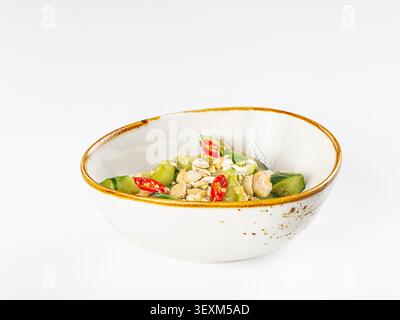 Frischer Gurkensalat mit gerösteten Erdnüssen in Scheiben geschnittenen roten Chili, serviert in rustikaler Keramikschale. Hellgrüne rote Farben stehen im Kontrast zu weißem Hintergrund. Clea Stockfoto