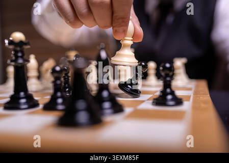 Die Hand schlägt eine schwarze Schachfigur mit einem weißen Schachstück um Stockfoto