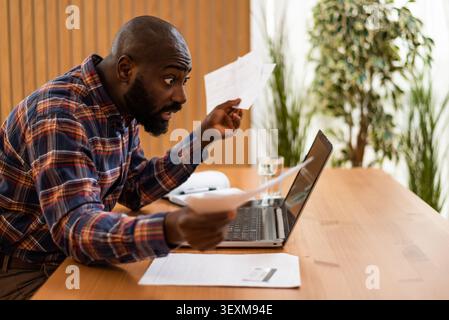 Von Papierkram überwältigt, kämpft ein Mann, um seine Finanzen zu organisieren, während er von zu Hause aus arbeitet. Stockfoto