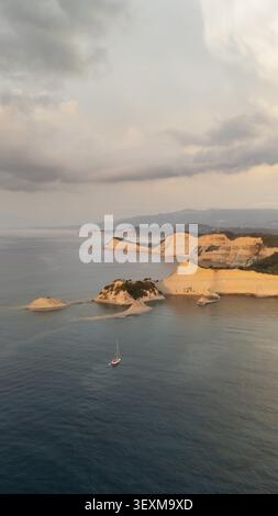 Aus der Vogelperspektive auf Kap Drastis mit dramatischen weißen Kalksteinklippen, türkisfarbenem Wasser und einem einsamen Segelboot im Ionischen Meer, Korfu, Griechenland. Stockfoto